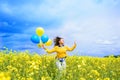 Yellow field with blooming rapeseed, a girl runs with balloons. The concept of freedom and summer.Yellow and blue Royalty Free Stock Photo