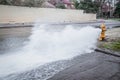 Yellow fire hydrant on corner of intersection gushing out water over road with large houses and trees in background Royalty Free Stock Photo