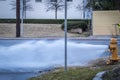 Yellow fire hydrant on corner of intersection gushing out water over road and man on other side with tool turning in manhole in Royalty Free Stock Photo