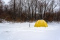 Yellow fishing winter tent stands with an ice-hole in the winter on the ice near the edge of the forest on a snow storm Royalty Free Stock Photo