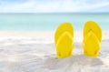 Yellow flip flops on beach sand texture and tropical sea background. Summer holidays and hot season. Fun ocean weekend. Summertime Royalty Free Stock Photo