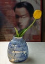 Yellow flower in Blue ceramic vase on white textured table cloth in front of Classic chinese poster movie frame