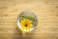 Yellow flower with green leaf floats in round glass vase with water on light brown wooden background, decoration of spa shop. Royalty Free Stock Photo