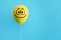 Yellow flying air helium balloon with smiling emoticon face against blue background. Happiness, positivity, optimism