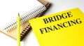 Yellow folder with the words bridge financing next to notebooks and pencil on white background Royalty Free Stock Photo