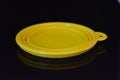 Yellow folding and multifunctional rubber plate, a bowl with a plastic edging on a black glossy surface.