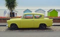Yellow Ford Anglia motor car on seafront road in front of beach huts. Royalty Free Stock Photo