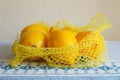 Yellow fresh lemons in plastic net on blue table cloth Royalty Free Stock Photo