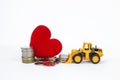 Yellow front loader moving stack of coins with pile of coins and red heart on background