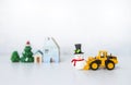 Yellow front loader truck toy with little snowman doll over blurred house and Christmas tree Royalty Free Stock Photo