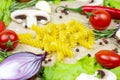 Yellow fusilli pasta and bright summer vegetables onion, garlic, tomato, pepper, rosemary and champignon mushroom on table