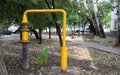 A yellow gas pipe with a valve stands in a public park