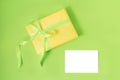 Yellow gift box with green silk ribbon and empty isolated label on pastel green background. Holiday gift concept. Flat