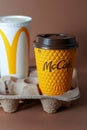 Yellow glass of coffee McDonald's. Paper glass drink Mc Cafe. Two cups on table. CocaCola and orange juice. Fastfood