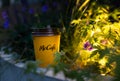 A yellow glass of McDonald's coffee next to the flowers.