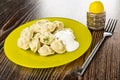 Yellow plate with dumplings poured sour cream, pepper shaker, fork on wooden table Royalty Free Stock Photo