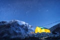 Yellow glowing tent against high rocks with snowy peak and sky w