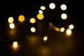 Yellow and gold lights garland in a blur on a black background. Bokeh of flying circles in the defocus. Festive atmosphere of Chri