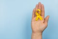 Yellow gold ribbon in the hand of a woman on a blue background. Children cancer concept. Awareness month. Childhood Cancer Day