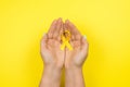 Yellow gold ribbon in the hands of a girl on a yellow background. Children cancer concept. Awareness month. Childhood Cancer Day