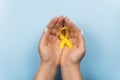 Yellow gold ribbon in the hands of a girl on a blue background. Children cancer concept. Awareness month. Childhood Cancer Day Royalty Free Stock Photo
