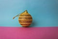 Yellow gold small round xmas festive Christmas ball, Christmas toy plastered over sparkles on a pink purple blue background Royalty Free Stock Photo