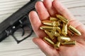 Yellow golden coloured bullets held in hand, blurred wooden desk with black gun under Royalty Free Stock Photo