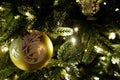 Yellow golden matte christmas ball with white ornament on a branch of christmas tree with lights bokeh background Royalty Free Stock Photo