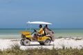 A yellow golf car cab on a tropical beach on the island of Holbox in Mexico, carrying tourists . In the background a the Caribbean