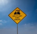 Yellow Golf Cart Crossing Sign With Black Letters Against A Blue Sky