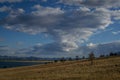 Yellow grassy coast with coniferous green trees of blue lake Baikal with mountains. Summer landscape with white clouds in sunset Royalty Free Stock Photo