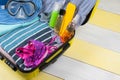 On a yellow-gray background, an open suitcase for traveling and a set of items for relaxing in it, a towel, a swimsuit, a hat, a