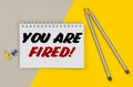 On a yellow-gray background are pencils, buttons and a notebook in which it is written - YOU ARE FIRED Royalty Free Stock Photo