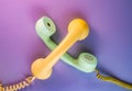 Yellow and green crossed telephone receivers with twisted cords from an old antique rotary phones on purple background