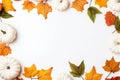 Yellow and green dried leaves and small orange pumpkins on white background, top view, copy space. Halloween, Thanksgiving holiday