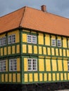 Yellow and green half-timbered building with row of windows and red shingles