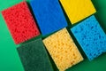 Yellow, green, red, blue sponges on green colored paper background, copy space, top view, flat lay