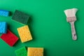 Yellow, green, red, blue sponges with paint brush on green colored paper background, copy space, top view, flat lay