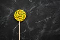 Yellow-green swirl lollipop on a black stone background. Spiral colored candy on a stick. Top view, flat lay, copy space