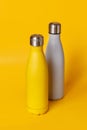 Yellow and grey reusable steel bottles on yellow background