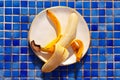 Yellow half peeled banana on the plate on blue ceramic tile mosaic background. Fresh organic fruit on sunny day. Close up. Flat Royalty Free Stock Photo