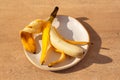 Yellow half peeled banana on the plate on brown background with sharp shadows. Fresh organic fruit on sunny day. Close up. Still Royalty Free Stock Photo