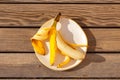 Yellow half peeled banana on the plate on wooden background with sharp shadows. Fresh organic fruit on sunny day. Close up. Flat Royalty Free Stock Photo