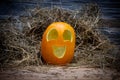 Yellow and happy smiling pumpkin. Halloween symbol on a gray stone wall background, stands on a hay and a wooden stand. Jack o Royalty Free Stock Photo