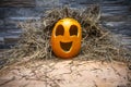 Yellow and happy smiling pumpkin. Halloween symbol on a gray stone wall background, stands on a hay and a wooden stand. Jack o Royalty Free Stock Photo