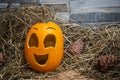 Yellow and happy smiling pumpkin. Halloween symbol on a gray stone wall background, stands on a hay and a wooden stand. Jack o Royalty Free Stock Photo