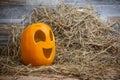 Yellow and happy smiling pumpkin. Halloween symbol on a gray stone wall background, stands on a hay and a wooden stand Royalty Free Stock Photo