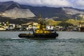 Yellow harbor tug close-up against the backdrop of the seaport and mountains. Royalty Free Stock Photo