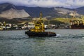 Yellow harbor tug close-up against the backdrop of the seaport and mountains. Royalty Free Stock Photo