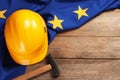 Yellow hard hat, hammer and flag of European Union on wooden table, flat lay. Space for text Royalty Free Stock Photo